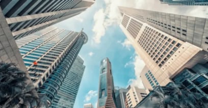 Tall modern skyscrapers viewed from below against a blue sky with scattered clouds.