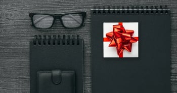 Black notebooks, eyeglasses, and a gift box with a red bow on a wooden desk.