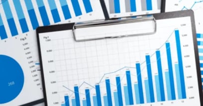 A collection of blue and white graphs on a clipboard displays various bar and line charts, conveying data analysis and business growth visually.