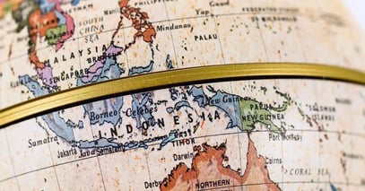 Close-up of a globe showing Southeast Asia, highlighting Indonesia, the Philippines, and Papua New Guinea. A horizontal brass ring frames the map.