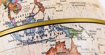 Close-up of a globe showing Southeast Asia, highlighting Indonesia, the Philippines, and Papua New Guinea. A horizontal brass ring frames the map.