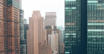 Tall city skyscrapers with glass and brick facades under a cloudy sky.