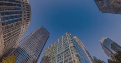 Fisheye view of tall city skyscrapers against a clear blue sky, with varied architecture and glass facades, conveying urban grandeur and vastness.