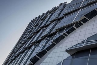 Modern glass and steel building facade with geometric architectural design, viewed from below.