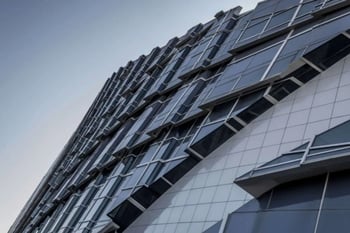 Modern glass and steel building facade with geometric architectural design, viewed from below.