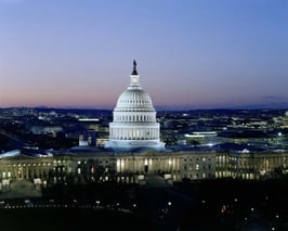 U.S. Capitol building illuminated at dusk with city lights in the background.