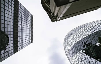 Looking up at modern glass skyscrapers against a cloudy sky.